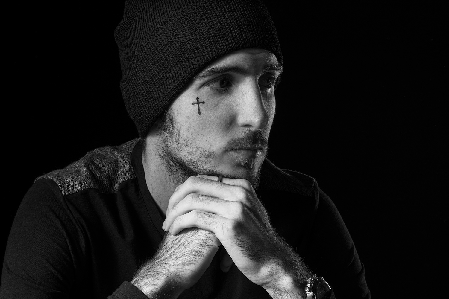 un homme tatoue avec un bonet et une montre en studio photo noir et blanc