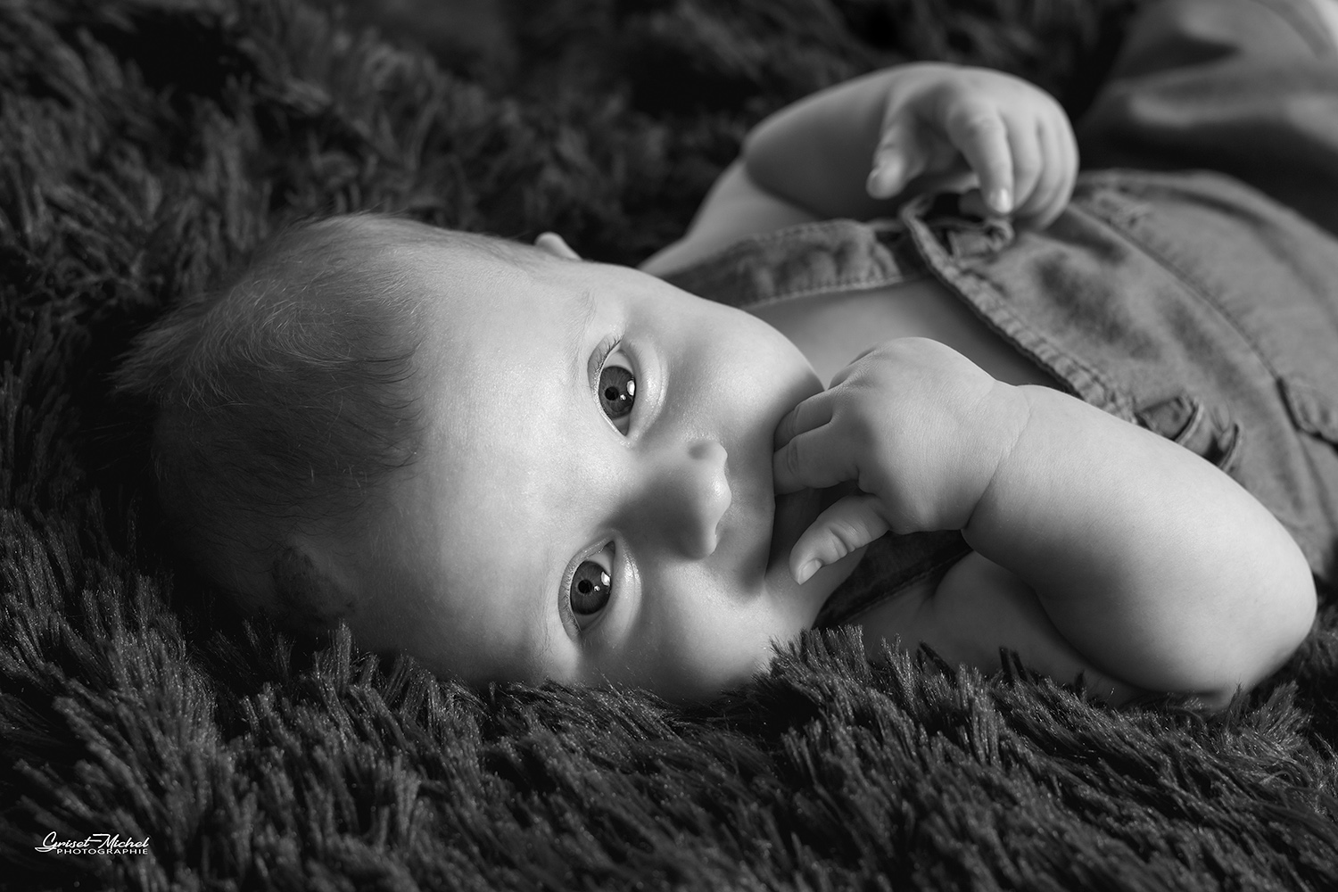 un bebe qui nous regard avec le doigt dans la bouche