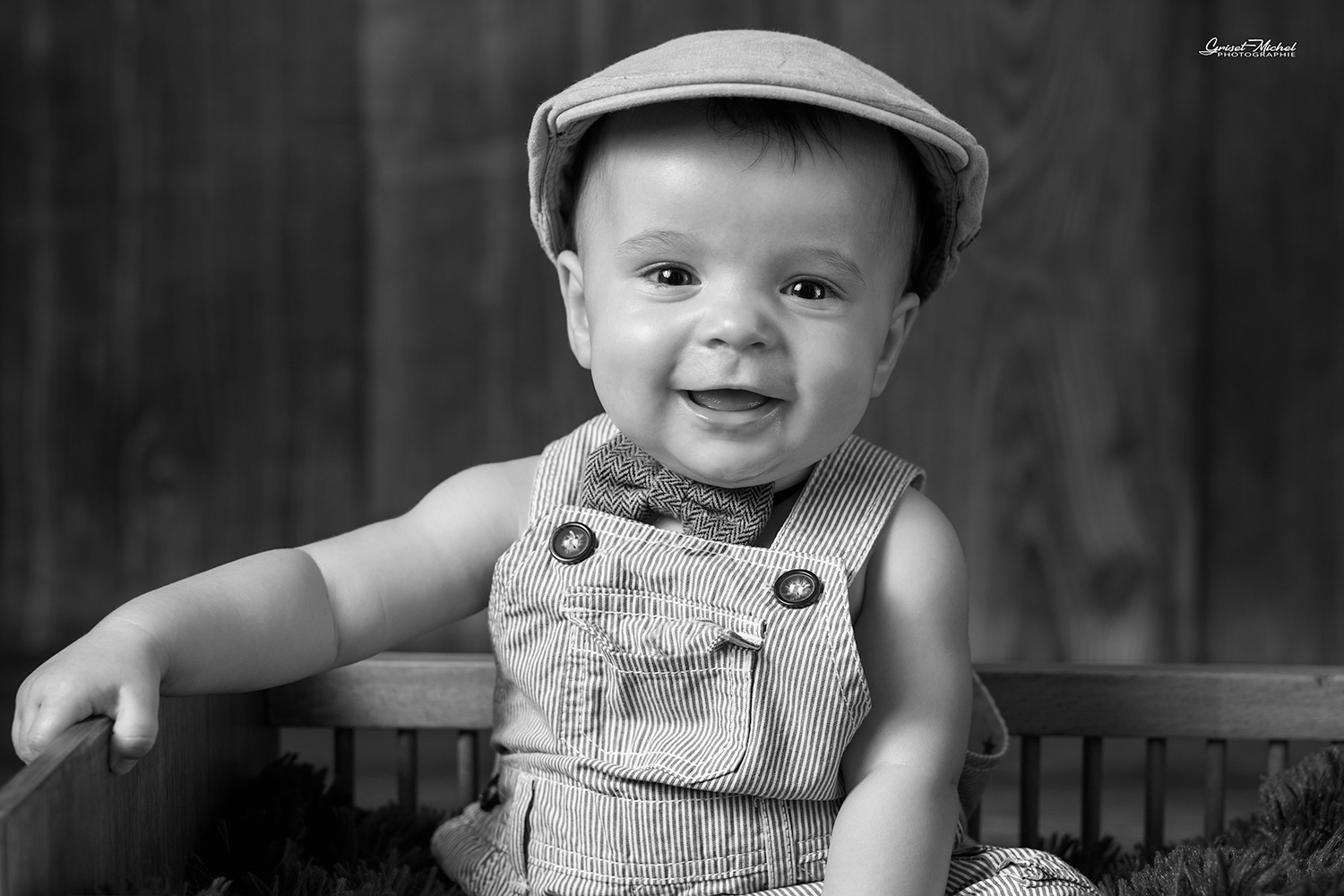 un bebe assis dans un lit avec un beret et un noeud de papillion