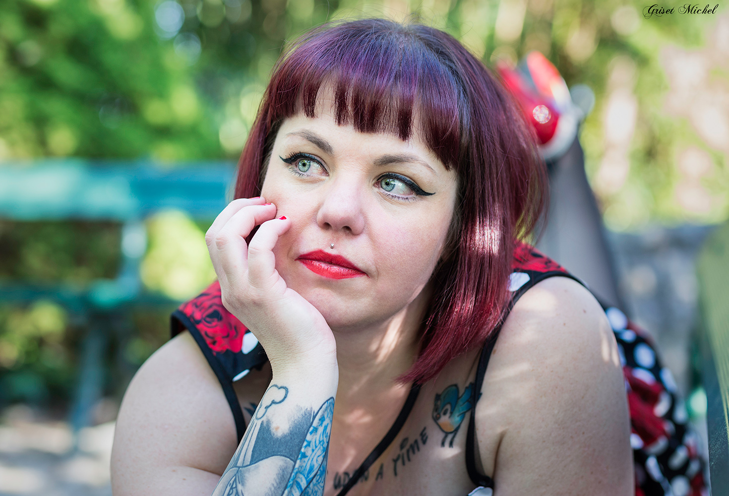 femme pin up allongee sur un banc la main sur sa joue avec un beau rouge a levre et des tatouages
