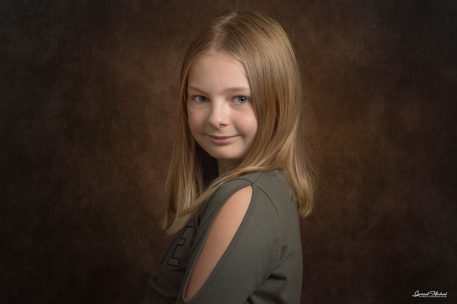 petite fille blonde avec un pull kaki sur un fond de studio rouge