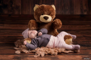 une petite fille avec un bonet en laine qui dort dans les bras de son ours en peluche