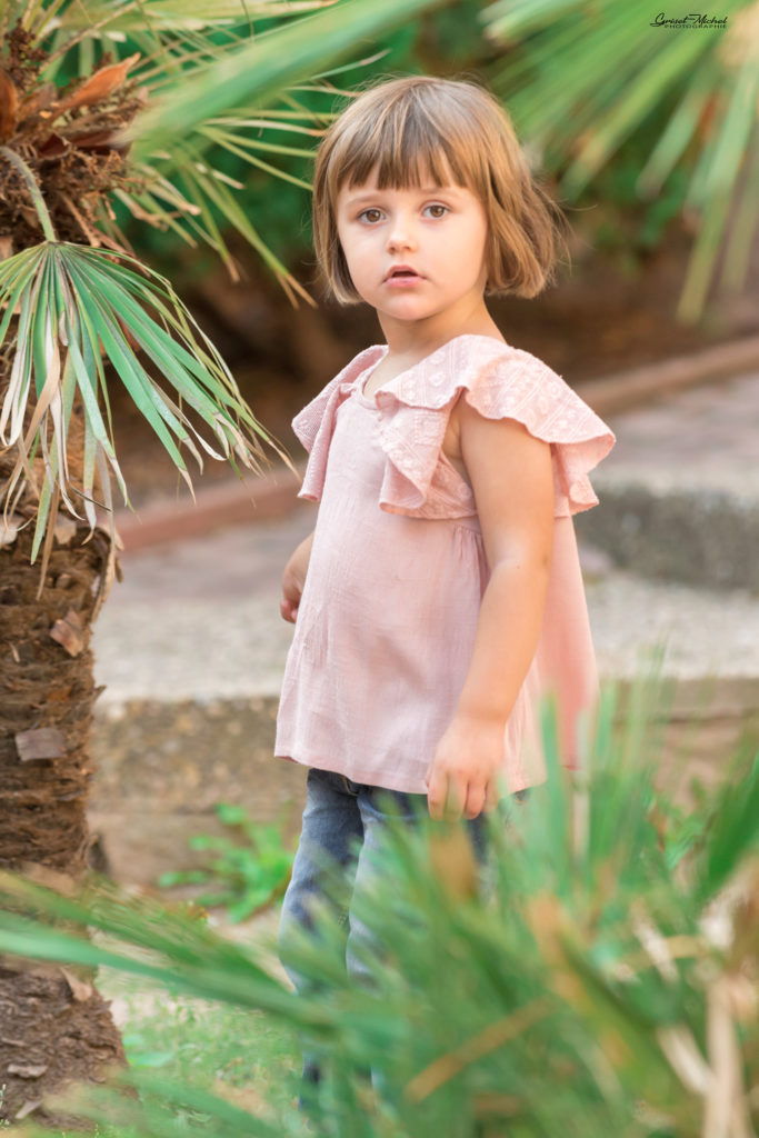 une petite fille au milieu des palmiers avec un t shirt rose
