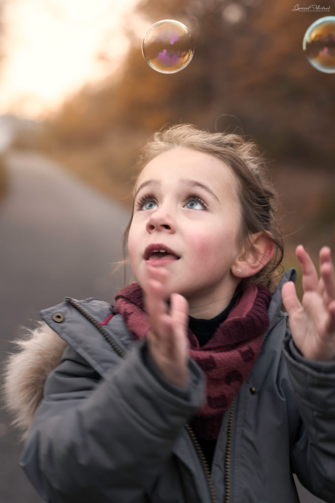 une petite fille joue avec des bulles dans un decor automnale
