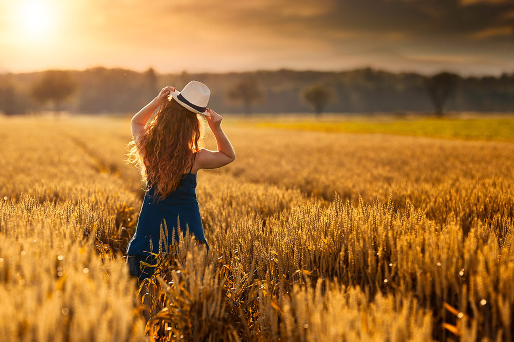 Un femme avec une robe bleu dans un champs avec un coucher du soleil
