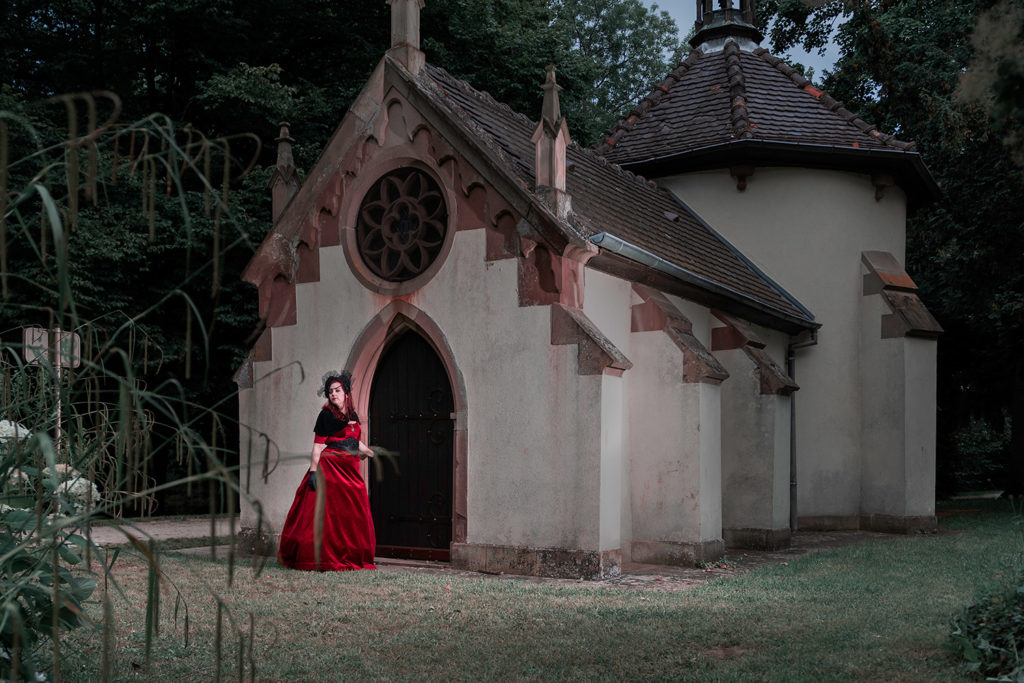 une femme avec une robe de creatrice rouge devant une eglis dans un parc a obernai