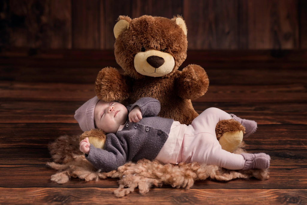 une petite fille avec un bonet en laine qui dort dans les bras de son ours en peluche