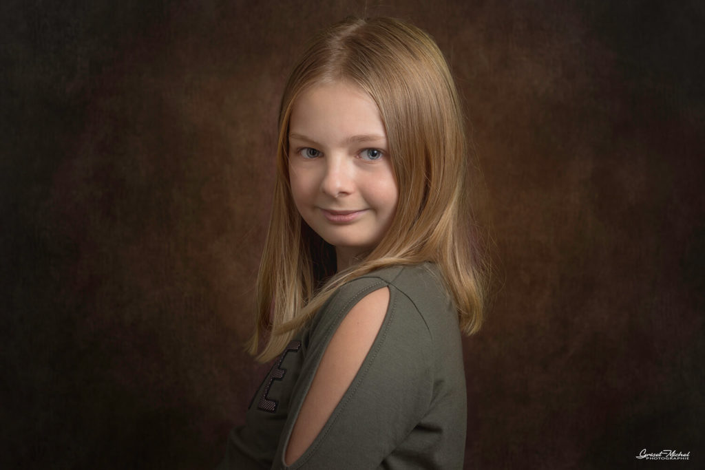 une petite fille blonde nous regarde en souriant en studio photo