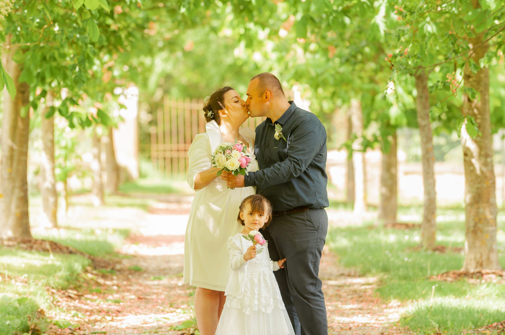 les maries s embrasse dans une allee d arbres avec leur petite fille un bouquet a la main