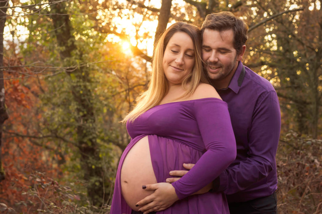 pendant un shooting photo de femme enceinte un couple s enlace dans un decor automnale avec un coucher du soleil
