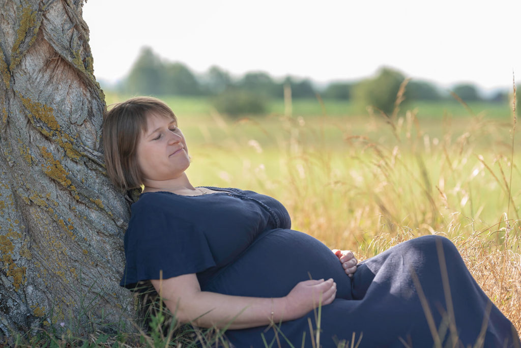 Seance grossesse en pleine nature une future maman contre un arbre avec les yeux fermes