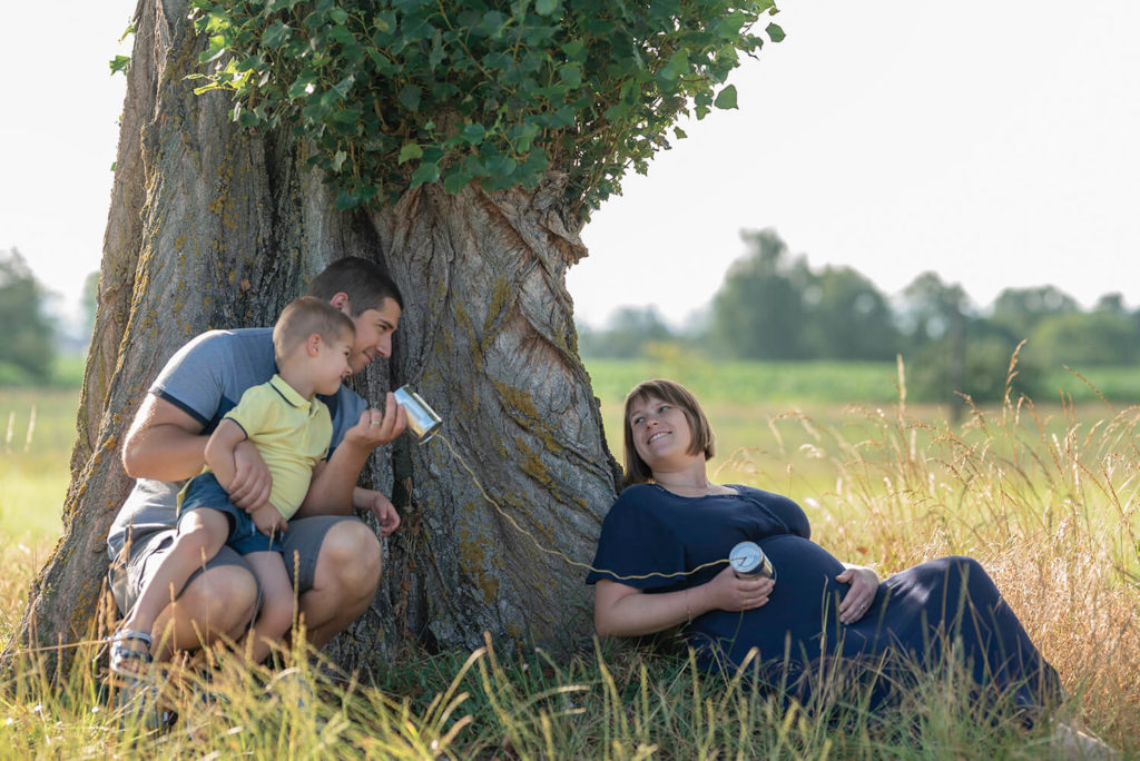 Seance grossesse une famille contre un arbre qui tiennent des converse en main en rigolant
