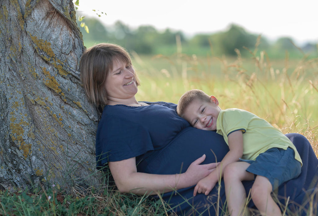Seance grossesse un petit garon pose sur sa maman qui rigole fort