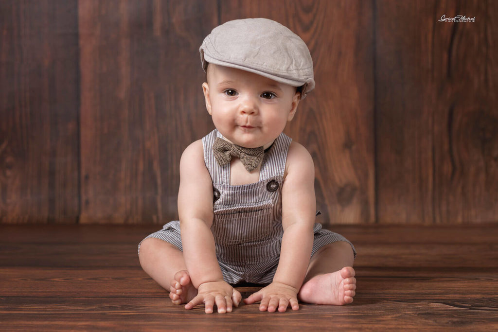 bebe assis avec un beret sur un fond en bois, , photographié par un photographe de bébé.