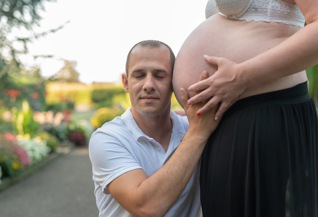 un homme colle son oreille contre le ventre de sa femme qui est enceinte