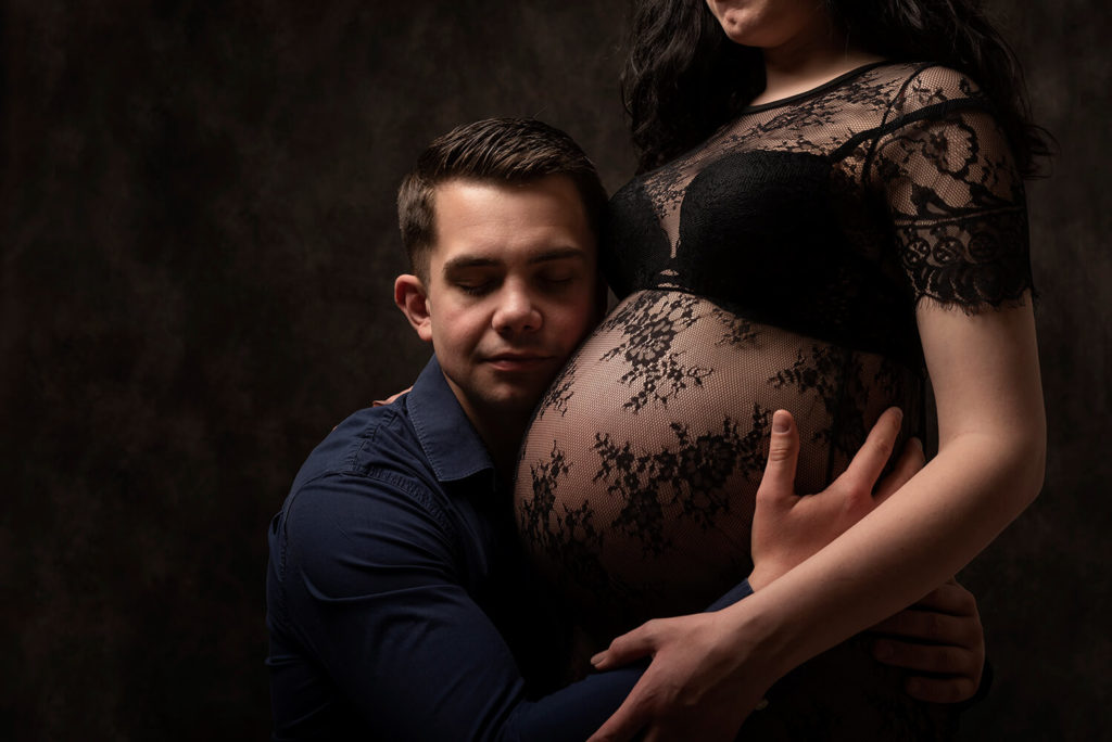 lors d'une séance photo chez le photographe à Sélestat un futur papa tiens le ventre rond de sa femme qui attend un bebe