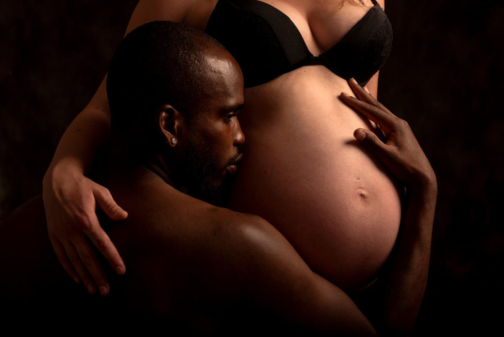 un homme qui tiens le ventre de sa femme enceinte en studio photo du photographe à Sélestat