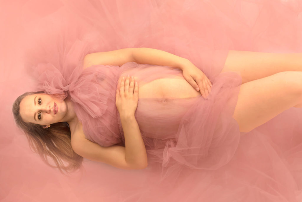 une femme enceinte allongée sur le sol avec une belle robe rose ouverte au niveau du ventre