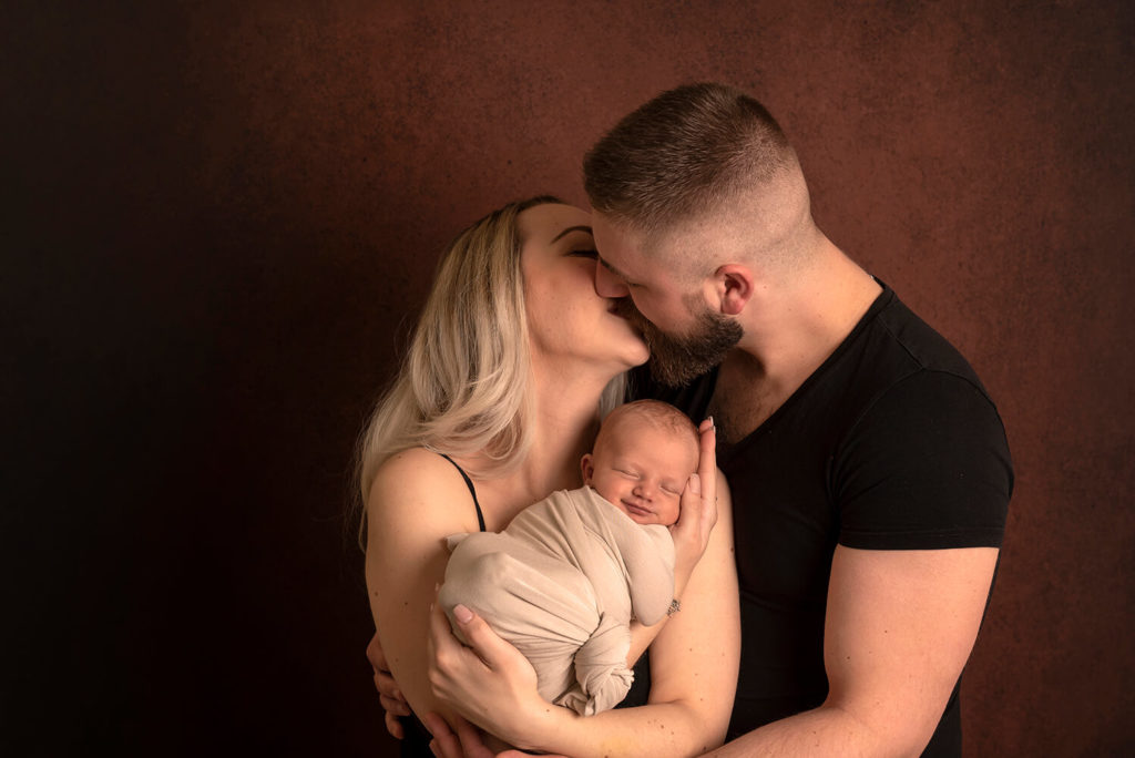 des jeunes parents s'embrasse pendant que leur petit bebe sourit photo dans un studio