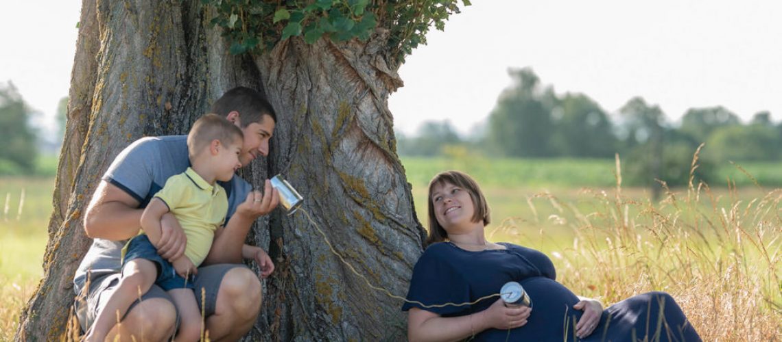 Seance grossesse une famille contre un arbre qui tiennent des converse en main en rigolant