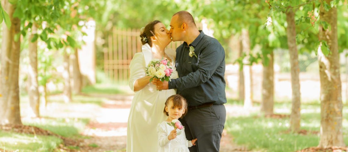 les maries s embrasse dans une allee d arbres avec leur petite fille un bouquet a la main